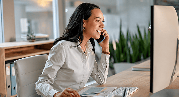 A smiling businesswoman talking on the phone while working at her desk.